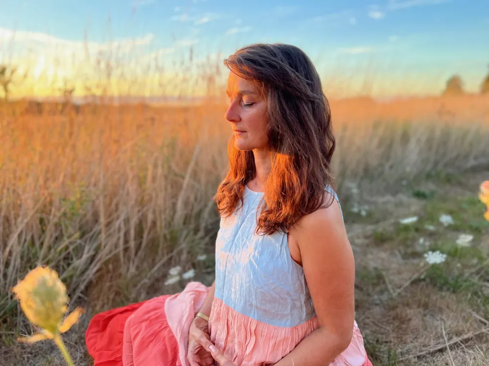 Alexandra Kalinine en méditation dans un champ au coucher du soleil